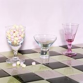Various stemmed glasses, one filled with sweets on chessboard patterned tiles