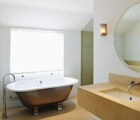 Modern stone sink and free-standing vintage bathtub with designer floor-mounted tap fittings