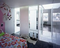 Flowered bed linen in child's room with view through ceiling-height window elements into stairwell and living room