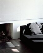 Wall panel with subtle white and pastel grey pattern above open fireplace next to modern black sofa