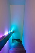 Durch indirekte Geländer-Beleuchtung in farbiges Licht getauchte Wände an schmalem Treppenaufgang