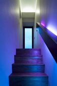 In farbiges Licht getauchter Treppenaufgang mit Holzstufen und Blick auf verglaste Zimmertür