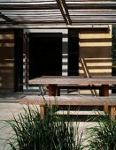Pattern of light and shade on plain, rustic dining area under wooden pergola