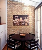 Round, black dining table in conservatory extension with modern photograph on brick wall