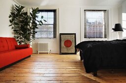Orange sofa and bed with black bedspread on rustic floorboards