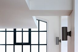 Ausschnitt einer abgehängten Decke vor Fenster mit schwarzen Sprossen und modernen Wandlampen