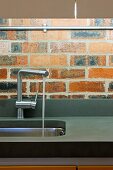 Designer tap fitting with water running into stainless steel sink in front of brick wall