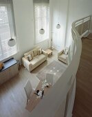 Blick von geschwungener Galerie auf offenen Wohnraum mit hellem modernem Sofa und Polstermöbel auf Parkett