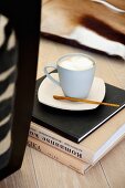 Capuccino Pause - Tasse auf Bücherstapel am Boden