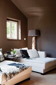 Elegant, white chaise longue below window in attic room painted dark brown