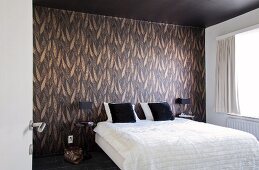 Comfortable double bed in bedroom with chocolate-brown ceiling and colour-coordinated leaf-patterned wallpaper