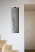 Sculpture in niche above wooden staircase in modern Maisonette apartment with doors of fitted cupboards in background