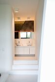 Steps leading to white ensuite bathroom with view of base cabinets with twin washbasins