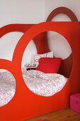 Child's bed with red, wooden, sculptural frame featuring large circular openings