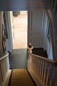 Old, renovated house in traditional, English country-house style; view down wooden staircase into hall with open door leading into living room