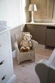 Teddy bear on child's wicker chair between turned lamp base and white, country-house chest of drawers