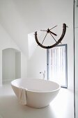 Free-standing, round bathtub below old ship's wheel in white bathroom