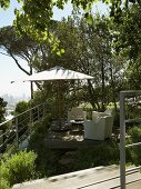 Outdoormöbel und Sonnenschirm auf Holzterrasse im mediterranen Garten