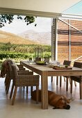 Wooden chairs with wicker seats and hand-crafted, modern wooden table on roofed terrace with amazing view of landscape