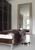 Chic dressing room with dark, glossy sliding doors on wardrobe, gigantic mirror and couch with animal-skin cover