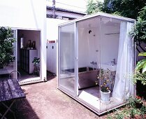 Teilweise verglaster Container mit Badeinrichtung im Garten aufgestellt