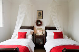 Twin beds with canopies and red scatter cushions in minimalist bedroom