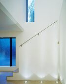 Double-height foyer with floor lights in front of white, masonry balustrade