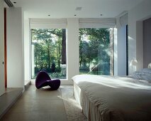 White bedroom with designer chaise longue in front of floor-to-ceiling terrace windows