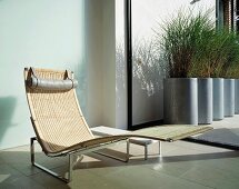 Designer rattan chaise longue in front of ceiling-height terrace door with view of planters