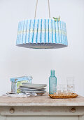Pendant lamp with retro paper shade above stacked plates next to tray of glasses on kitchen table