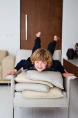 Child lying on stack of cushions on ecru armchair