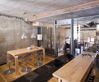 Holztische mit Designer-Stühlen in einer Küche mit Beton- und Glaswänden