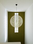 Spherical, designer pendant lamp made from pale mesh in front of green-painted wall with strip of glass bricks in stairwell