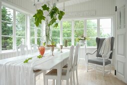 White dining table and chairs and reading chair in loggia of white wooden house