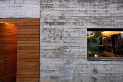 Contemporary house facade in Brutalist style with horizontal window and wood-clad entrance