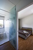 View into modern bedroom with strip parquet, glass door and ensuite bathroom