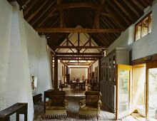 Antique armchairs on terracotta floor beneath historic roof timbers contrasting with yellow, modern terrace door
