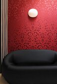 Black designer sofa in front of red wallpaper with traditional, floral pattern