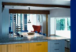 Blick über moderne Küchenzeile mit farbigen Holzfronten und Granit-Arbeitsplatte auf Essplatz mit Fifties-Stühlen