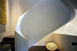 Sculptural spiral staircase with white, masonry balustrade, artwork with text motif and egg-shaped floor lamp