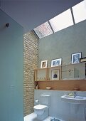 A light bathroom with a brick wall, framed photos and a large skylight