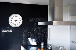 Station clock hanging on black wall with lettering above kitchen island
