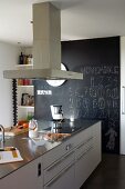 Küchenblock mit Dunstabzug in moderner Küche; dahinter eine wandhohe schwarze Schiefertafel