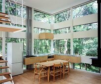 Kitchen with dining area in house made of glass and wood elements in forest