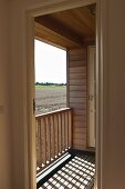 Modernes Holzhaus mit kleinem Balkon - Sonneneinfall durch Geländer und Blick auf Ackerlandschaft