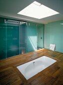 Skylight above sunken bathtub in wooden floor and bluish glass sliding doors in ensuite designer bathroom
