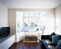 Stilmix im Wohnzimmer - modernes Ledersofa kombiniert mit Sitzplatz im Fenstererker auf Überseekoffer