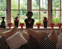 Various scatter cushions in front of windowsill with male bust and pots