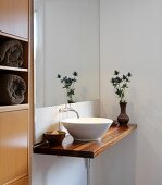 Minimalist washstand with white ceramic basin on wooden counter in corner of bathroom