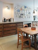 Rustic dining table in front of kitchen unit and collection of plates on wall